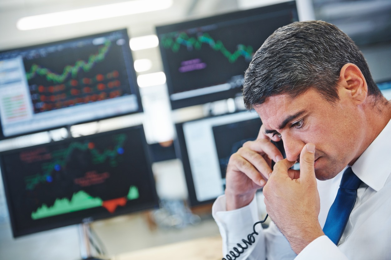 Profile shot of a concerned businessman talking on the phone while sitting in front of monitors displaying financial information